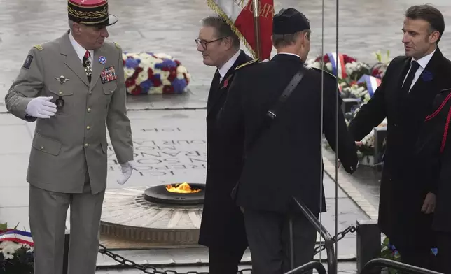 French President Emmanuel Macron, right, and British Prime Minister Keir Starmer, center, walk past the flame of the Tomb of the Unknown Soldier during ceremonies marking the 106th anniversary of the Armistice, a celebration of their countries' friendship, as nations across the world pay tribute to their fallen soldiers in World War I, Monday, Nov. 11, 2024 in Paris, (AP Photo/Michel Euler, Pool)