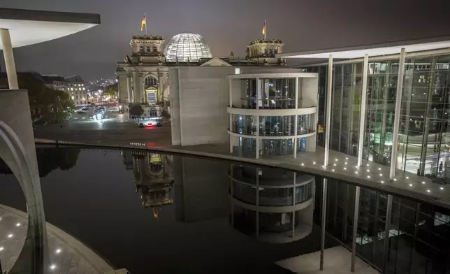 Parts of the Reichstag building with the Bundestag and the Paul Löbe House in Berlin's government district are reflected in the Spree at night, early Thursday, Nov. 7, 2024. (Kay Nietfeld/dpa via AP)