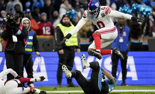 New York Giants linebacker Brian Burns jumps over Carolina Panthers running back Chuba Hubbard during the first half of an NFL football game, Sunday, Nov. 10, 2024, in Munich, Germany. (AP Photo/Matthias Schrader)