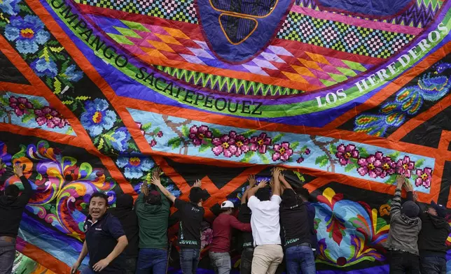 People help lift a giant kite to be displayed on All Saints Day as part of Day of the Dead celebrations in Sumpango, Guatemala, Friday, Nov. 1, 2024. (AP Photo/Matias Delacroix)