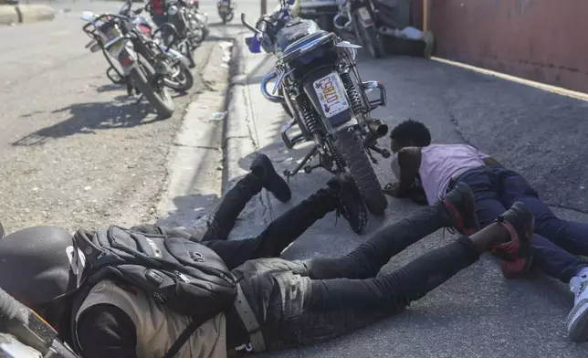 People take cover from the exchange of gunfire between Gangs and police in Port-au-Prince, Haiti, Monday, Nov. 11, 2024. (AP Photo/Odelyn Joseph)