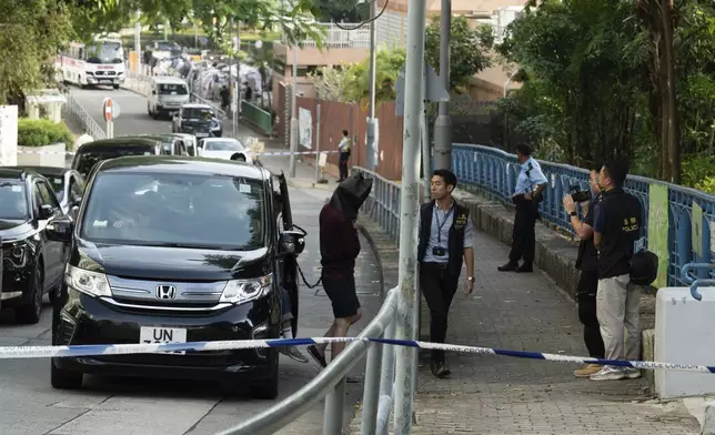 An unidentified person wearing a hood is escorted by police officers to a park for video reconstruction of a crime scene where a Southeast Asian woman's body was found Monday at a waterfall inside the park in Hong Kong, Wednesday, Oct. 30, 2024. (AP Photo/Bertha Wang)