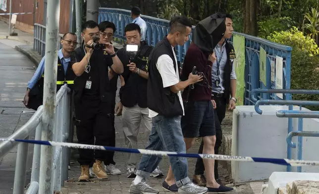 An unidentified person wearing a hood is escorted by police officers to a park for video reconstruction of a crime scene where a Southeast Asian woman's body was found Monday at a waterfall inside the park in Hong Kong, Wednesday, Oct. 30, 2024. (AP Photo/Bertha Wang)