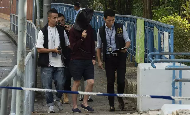 An unidentified person wearing a hood is escorted by police officers to a park for video reconstruction of a crime scene where a Southeast Asian woman's body was found Monday at a waterfall inside the park in Hong Kong, Wednesday, Oct. 30, 2024. (AP Photo/Bertha Wang)