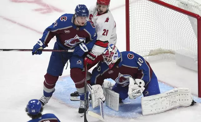 The puck bounces off Carolina Hurricanes center Sebastian Aho, center, and over Colorado Avalanche goaltender Alexandar Georgiev, right, in the first period of an NHL hockey game as Aho fights for position in front of the net with Colorado defenseman Josh Manson Saturday, Nov. 9, 2024, in Denver. (AP Photo/David Zalubowski)