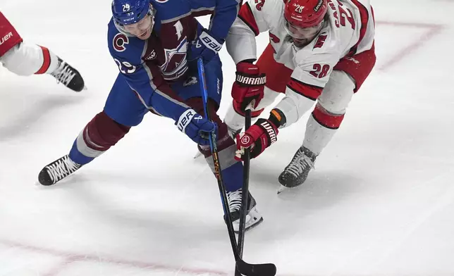 Colorado Avalanche center Nathan MacKinnon, left, struggles to control the puck as Carolina Hurricanes left wing William Carrier defends in the first period of an NHL hockey game Saturday, Nov. 9, 2024, in Denver. (AP Photo/David Zalubowski)