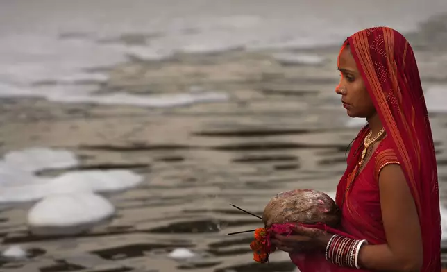 A devotee prays on the banks of the river Yamuna as toxic foam flows during Chhath festival in Noida, near New Delhi, India, Thursday, Nov. 7, 2024. (AP Photo/Manish Swarup)