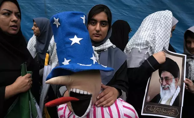 A schoolgirl holds an effigy of the Uncle Sam as another one holds a poster of the Iranian Supreme Leader, Ayatollah Ali Khamenei, in an annual rally in front of the former U.S. Embassy in Tehran, Iran, Sunday, Nov. 3, 2024, marking the 45th anniversary of Iranian students' takeover of the embassy, starting a hostage crisis. (AP Photo/Vahid Salemi)