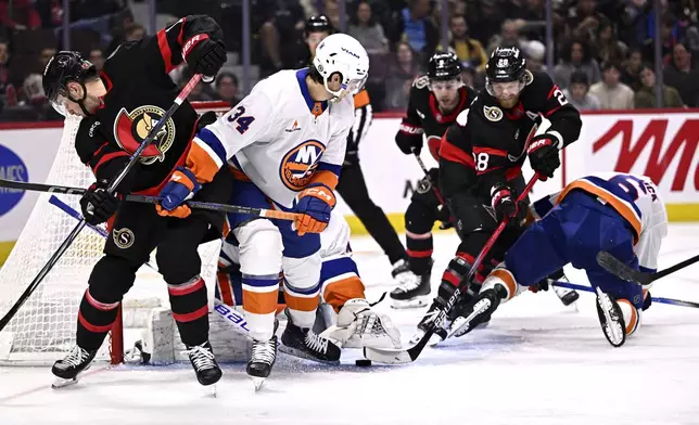 The glove of New York Islanders goaltender Semyon Varlamov, centre hidden, reaches out to make the save as Ottawa Senators right wing Drake Batherson (left), right wing Claude Giroux (28), and Islanders defenceman Grant Hutton (34) look for the puck, during second period NHL hockey action in Ottawa, on Thursday, Nov. 7, 2024. (Justin Tang/The Canadian Press via AP)