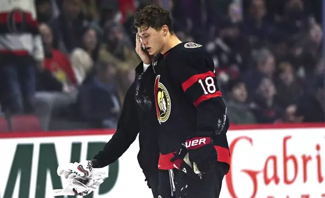 Ottawa Senators centre Tim Stutzle (18) is helped off the ice by a trainer after taking a puck to the face during first period NHL hockey action against the New York Islanders in Ottawa, on Thursday, Nov. 7, 2024. (Justin Tang/The Canadian Press via AP)