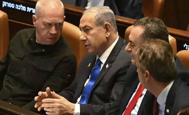 Israeli Prime Minister Benjamin Netanyahu, center, speaks to Defense Minister Yoav Gallant, left, at the opening of the 25th Knesset session marking the anniversary of the "Iron Swords" war, in Jerusalem, Monday, Oct. 28, 2024. (Debbie Hill/Pool Photo via AP)