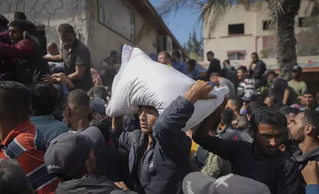 Palestinians gather to receive bags of flour distributed by UNRWA, the U.N. agency helping Palestinian refugees, in Deir al Balah, central Gaza Strip, Saturday, Nov. 2, 2024. (AP Photo/Abdel Kareem Hana)