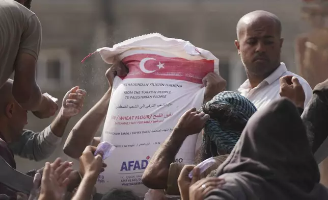 Palestinians gather to receive bags of flour distributed by UNRWA, the U.N. agency helping Palestinian refugees, in Deir al Balah, central Gaza Strip, Saturday, Nov. 2, 2024. (AP Photo/Abdel Kareem Hana)