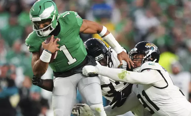 Philadelphia Eagles quarterback Jalen Hurts (1) scrambles under pressure from Jacksonville Jaguars linebacker Devin Lloyd, center, and Jaguars defensive end Arik Armstead during the first half of an NFL football game Sunday, Nov. 3, 2024, in Philadelphia. (AP Photo/Matt Slocum)
