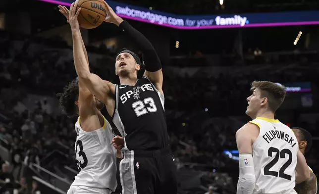 San Antonio Spurs' Zach Collins (23) goes to the net against Utah Jazz's Johnny Juzang, left, and Kyle Filipowski (22) during the first half of an NBA basketball game, Saturday, Nov. 9, 2024, in San Antonio. (AP Photo/Darren Abate)