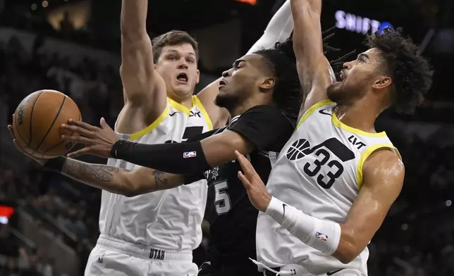 San Antonio Spurs' Stephon Castle (5) goes to the basket against Utah Jazz's Johnny Juzang (33) and Walker Kessler, left, during the first half of an NBA basketball game, Saturday, Nov. 9, 2024, in San Antonio. (AP Photo/Darren Abate)