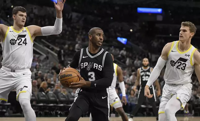 San Antonio Spurs' Chris Paul (3) looks to pass the ball as he is defended by Utah Jazz's Lauri Markkanen (23) and Walker Kessler (24) during the first half of an NBA basketball game, Saturday, Nov. 9, 2024, in San Antonio. (AP Photo/Darren Abate)