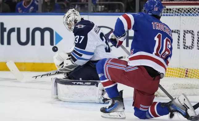 Winnipeg Jets goaltender Connor Hellebuyck, left, makes a save as New York Rangers' Vincent Trocheck looks on during the first period of an NHL hockey game Tuesday, Nov. 12, 2024, in New York. (AP Photo/Seth Wenig)