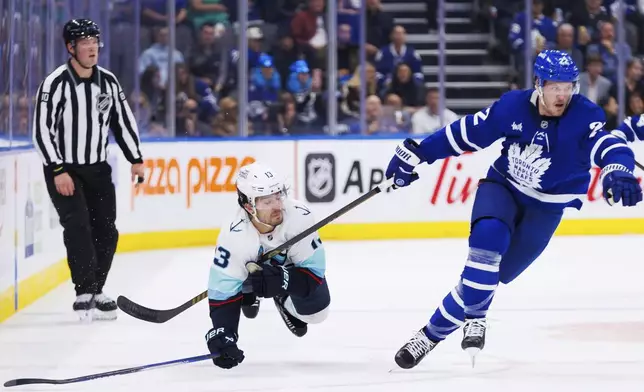 Seattle Kraken left wing Brandon Tanev (13) falls on the stick of Toronto Maple Leafs defenseman Jake McCabe (22) during the first period of an NHL hockey game, Thursday, Oct. 31, 2024 in Toronto. (Cole Burston/Canadian Press via AP)