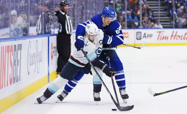 Toronto Maple Leafs center David Kampf (64) reaches over top of Seattle Kraken right wing Jordan Eberle (7) as they battle for the puck during the first period of an NHL hockey game, Thursday, Oct. 31, 2024 in Toronto. (Cole Burston/Canadian Press via AP)