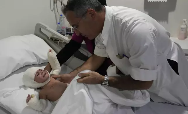 Plastic surgeon doctor Ziad Sleiman, inspects Ivana Skakye, 2, a Lebanese child who is suffering from third-degree burns over 40 percent of her body following an Israeli airstrike last September near their home in Deir Qanoun al Nahr a village in south Lebanon, as she lies on a bed at the Geitaoui hospital where she is receiving treatment, in Beirut, Lebanon, Tuesday, Oct. 29, 2024. (AP Photo/Hussein Malla)