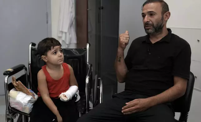 Hussein Mikdad, 4, left, who was injured on Oct. 2 in an Israeli airstrike at a densely-populated neighborhood south of Beirut, looks at his father Hassan, during an interview with The Associated Press at the American University of Beirut Medical Center (AUBMC), in Beirut, Lebanon, Tuesday, Nov. 5, 2024. (AP Photo/Bilal Hussein)