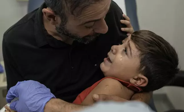 Hassan Mikdad, holds his son Hussein Mikdad, 4, who was injured on Oct. 2 in an Israeli airstrike at a densely-populated neighborhood south of Beirut, as he cries during a check up by his doctor at the American University of Beirut Medical Center (AUBMC), in Beirut, Lebanon, Tuesday, Nov. 5, 2024. (AP Photo/Bilal Hussein)