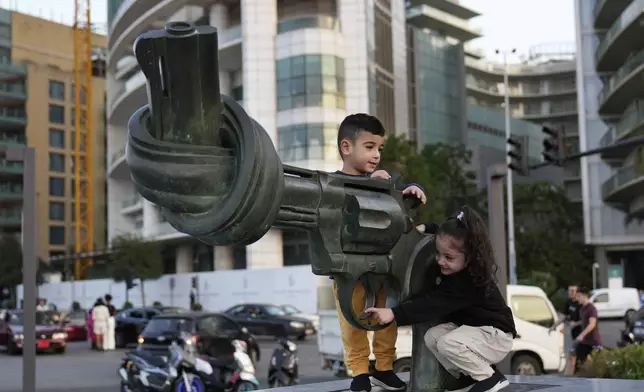 Hussein and Zahraa, 3, displaced Lebanese twins who fled with their parents from their village of Mais al-Jabal in south Lebanon amid the ongoing Hezbollah-Israel war, play on a gun with a twisted barrel statute, symbolizing anti-violence, in Beirut, Lebanon, Thursday, Oct. 31, 2024. (AP Photo/Hussein Malla)