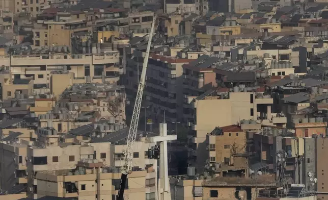 Workers in a crane basket, fix the giant cross of Our Lady of Hadath Church, with Dahiyeh, the southern suburb of Beirut seen in the background, Lebanon, Friday, Nov. 1, 2024. (AP Photo/Hussein Malla)