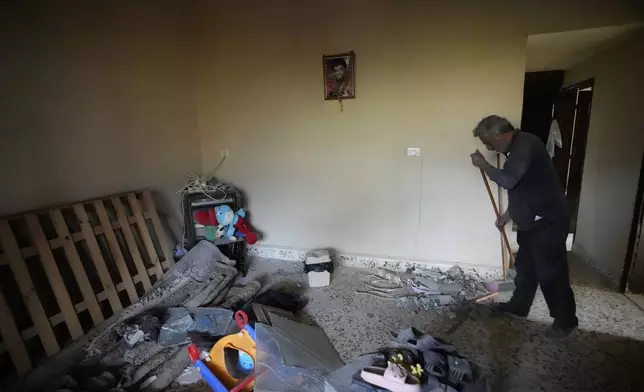 A man cleans a house, as a portrait hanging on the wall shows the late Hezbollah leader Sayyed Hassan Nasrallah, at the site where an Israeli airstrike hit a house in Aalmat village, northern Lebanon, Sunday, Nov. 10, 2024. (AP Photo/Hassan Ammar)