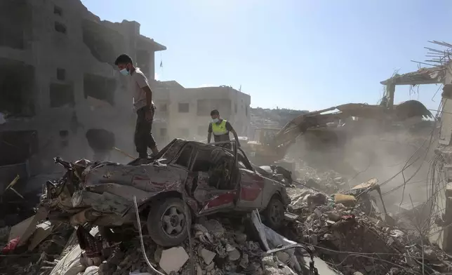 Rescue worker stand on a destroyed car over the rubble of a destroyed building hit by an Israeli airstrike in Saksakiyeh village, south Lebanon, Tuesday, Nov. 12, 2024. (AP Photo/Mohammed Zaatari)