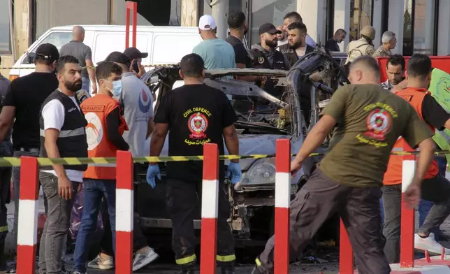 In this handout photo, civil defense workers and paramedics stand next to a charred car in an Israeli airstrike at the entrance of the southern port city of Sidon, Lebanon, Thursday, Nov. 7, 2024. (AP Photo)