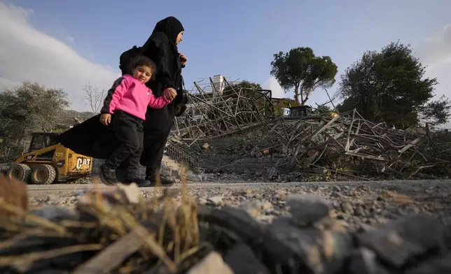 A woman with a child pass at the site where an Israeli airstrike hit a house in Aalmat village, northern Lebanon, Sunday, Nov. 10, 2024. (AP Photo/Hassan Ammar)