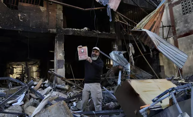 A man holds up a portrait of the late revolutionary founder Ayatollah Khomeini under a destroyed building that was hit by an Israeli airstrike in Dahiyeh, in the southern suburb of Beirut, Lebanon, Monday, Nov. 11, 2024. (AP Photo/Hussein Malla)