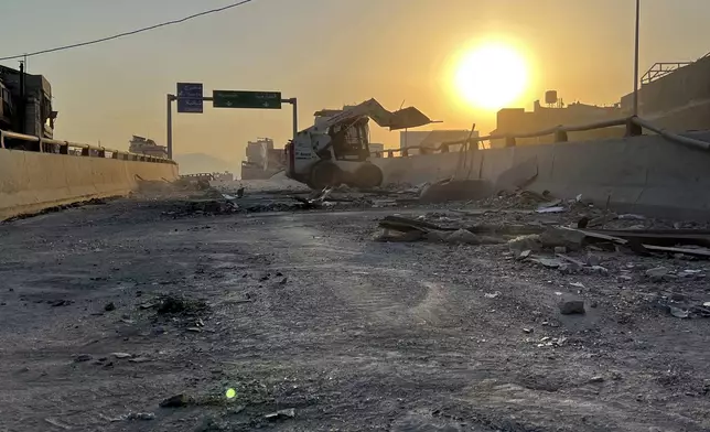 A municipality worker uses a skid steer loader to reopen a bridge closed by the rubble of a destroyed building that was hit by an Israeli airstrike on Dahiyeh, as the sunrise in the southern suburb of Beirut, Lebanon, Friday, Nov. 1, 2024. (AP Photo/Hussein Malla)