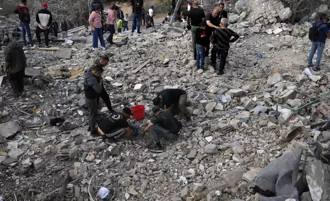 Rescue workers and people, centre, search for victims under the rubble of a destroyed house hit in an Israeli airstrike, in Aalmat village, northern Lebanon, Sunday, Nov. 10, 2024. (AP Photo/Hassan Ammar)