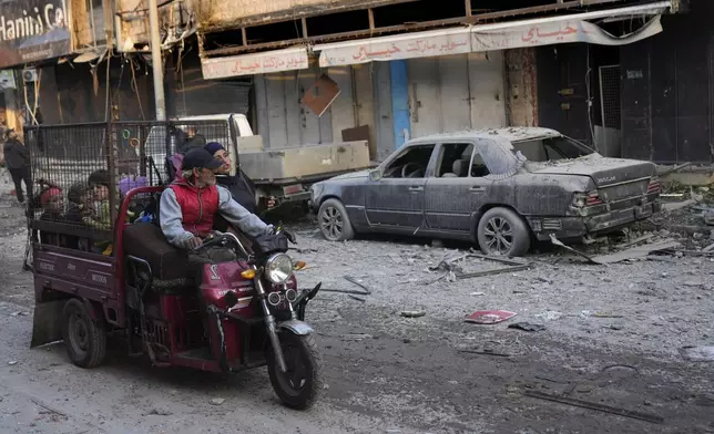 A man rides with his family a three-wheeled motorized known as "tok-toks," as they pass by a car that was damaged after an Israeli airstrike hit a building on Dahiyeh, in the southern suburb of Beirut, Lebanon, Friday, Nov. 1, 2024. (AP Photo/Hussein Malla)