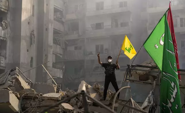 A man flashes the victory sign as holds up a Hezbollah flag while stands on the ruins of his destroyed apartment at the site of an Israeli airstrike in Dahiyeh, Beirut, Lebanon, Friday, Nov. 1, 2024. (AP Photo/Hassan Ammar)