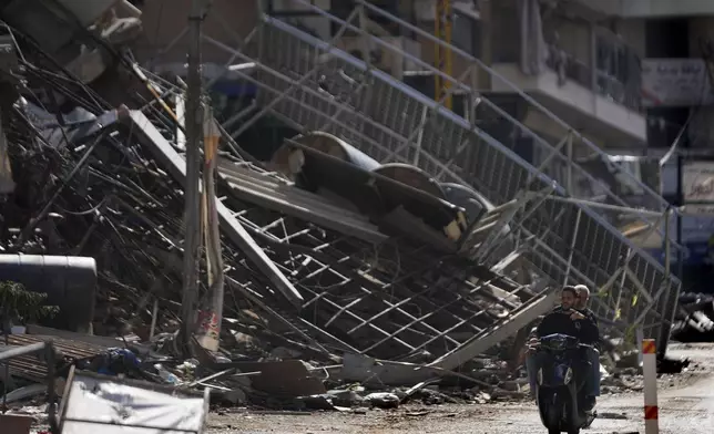 Two men ride a scooter past a building that was destroyed by an Israeli airstrike in Dahiyeh, in the southern suburb of Beirut, Lebanon, Monday, Nov. 11, 2024. (AP Photo/Hussein Malla)