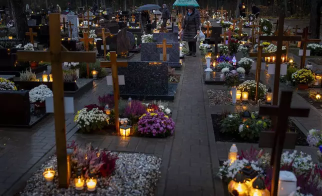 People light candles over graves during All Saints Day, a Catholic ceremony to reflect on the saints and deceased relatives, in Vilnius, Lithuania, Friday, Nov. 1, 2024. (AP Photo/Mindaugas Kulbis)