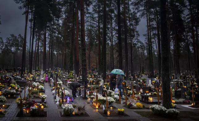 People light candles over graves during All Saints Day, a Catholic ceremony to reflect on the saints and deceased relatives, in Vilnius, Lithuania, Friday, Nov. 1, 2024. (AP Photo/Mindaugas Kulbis)