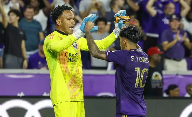 Orlando City goalkeeper Pedro Gallese, left, congratulates teammate forward Facundo Torres, right, after scoring one of the goals in the shoot-out against Charlotte FC after the end of regulation play of Game 3 in the first round MLS Cup playoff soccer match Saturday, Nov. 9, 2024, in Orlando, Fla. (AP Photo/Kevin Kolczynski)