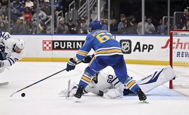 St. Louis Blues' Jake Neighbours (63) reaches for the puck as Toronto Maple Leafs' goaltender Joseph Woll (60) lies on the ice during the second period of an NHL hockey game Saturday, Nov. 2, 2024, in St. Louis. (AP Photo/Connor Hamilton)