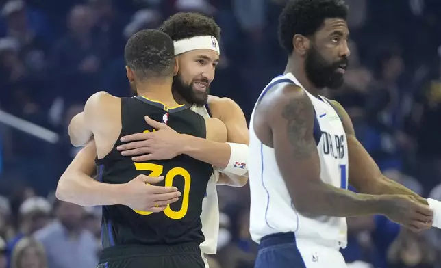 Golden State Warriors guard Stephen Curry, left, hugs Dallas Mavericks guard Klay Thompson, middle, as guard Kyrie Irving, right, walks on the court before an Emirates NBA Cup basketball game in San Francisco, Tuesday, Nov. 12, 2024. (AP Photo/Jeff Chiu)