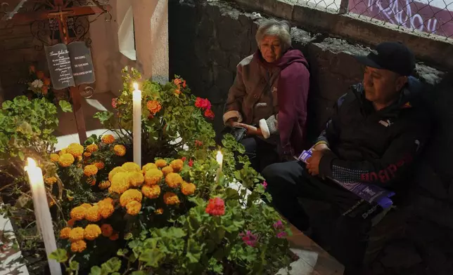 Juana Godoy, left, and Isaac Gonzalez sit at the tomb of their dearly departed, as they celebrate the Day of the Dead, at the San Gregorio Atlapulco cemetery on the outskirts of Mexico City, Friday, Nov. 1, 2024. (AP Photo/Moises Castillo)