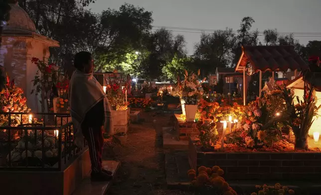 A woman stands at a tomb of a dearly departed, celebrating Day of the Dead, at the San Gregorio Atlapulco cemetery on the outskirts of Mexico City, Friday, Nov. 1, 2024. (AP Photo/Moises Castillo)