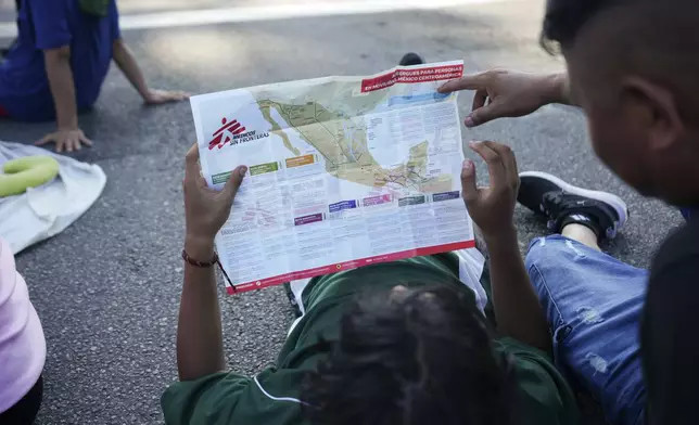 Migrants, who are part of a a caravan heading toward the country's northern border and ultimately the United States, check a map during a break, on the outskirts of Escuintla, southern Mexico, Thursday, Nov. 7, 2024. (AP Photo/Moises Castillo)