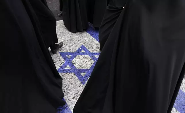 Women walk on an image of the Israeli flag put on the street in an annual rally in front of the former U.S. Embassy in Tehran, Iran, Sunday, Nov. 3, 2024, marking the 45th anniversary of Iranian students' takeover of the embassy, starting a hostage crisis. (AP Photo/Vahid Salemi)