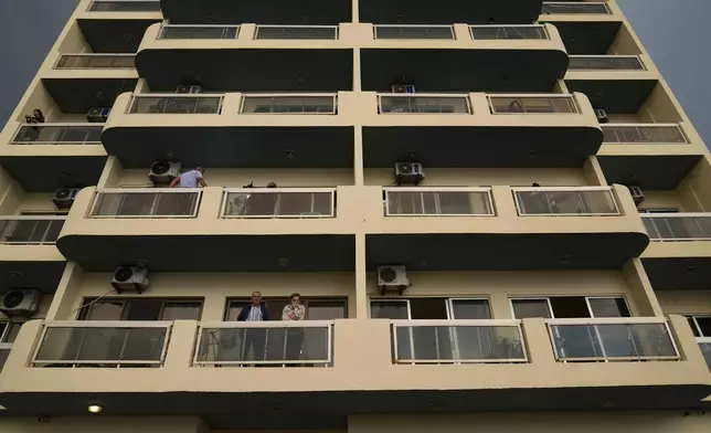 Residents stand on the balcony of a building in Batroun, northern Lebanon, Saturday, Nov. 2, 2024, where Lebanese officials say a ship captain was taken away by a group of armed men who landed on a coast north of Beirut and they're investigating whether Israel was involved. (AP Photo/Hussein Malla)