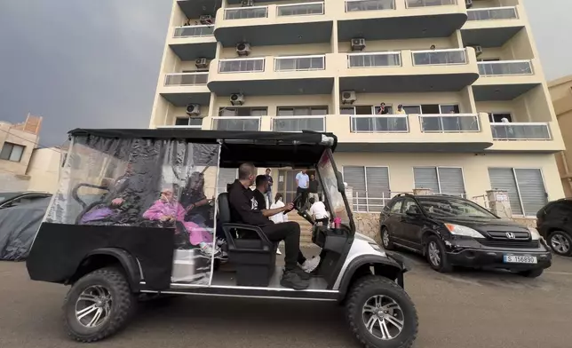 Residents ride a golf cart, as they pass in front of a building in Batroun, northern Lebanon, Saturday, Nov. 2, 2024, where Lebanese officials say a ship captain was taken away by a group of armed men who landed on a coast north of Beirut and they're investigating whether Israel was involved. (AP Photo/Hussein Malla)